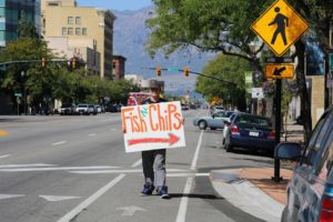 Man holding a Fish 'n' Chips sign on a street - one of the ways to promote your business for free.