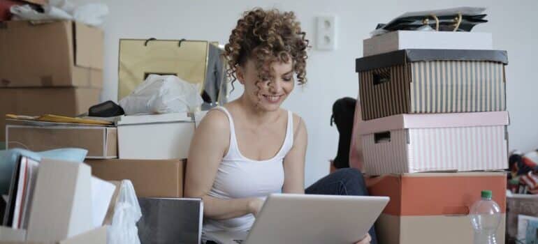 Woman surrounded by boxes, looking at her laptop