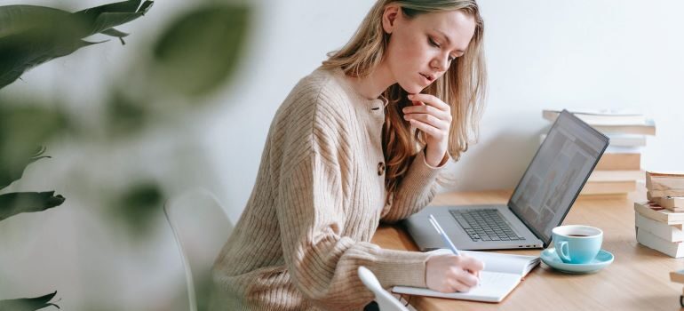 Woman taking notes next to a laptop.
