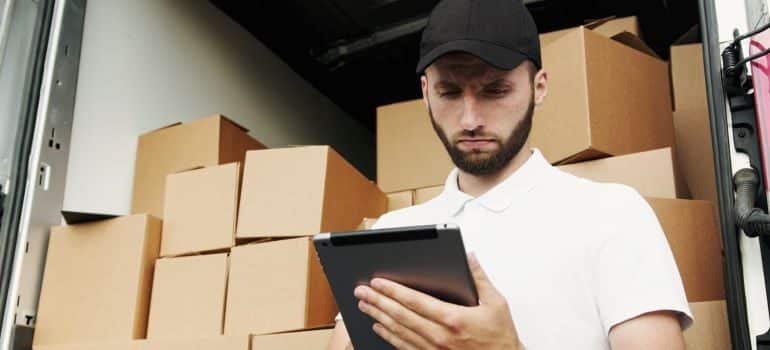 Man holding a tablet, with a truck filled with moving boxes behind him.