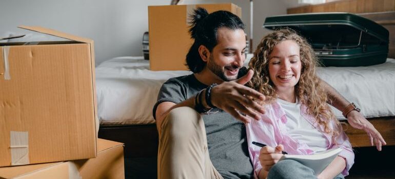 A couple looking for moving companies while smiling and surrounded by moving boxes.