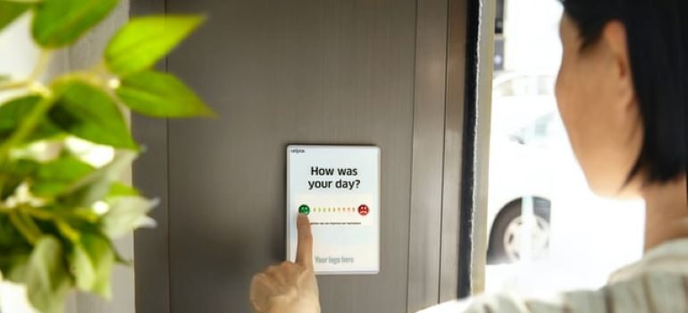 A woman answering a survey on a tablet that's attached to the brown door next to a hanging house plant