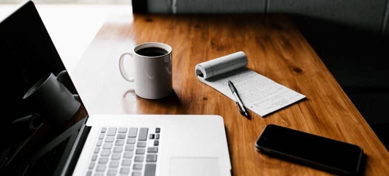 Laptop, coffee cup, writing pad, and smartphone.