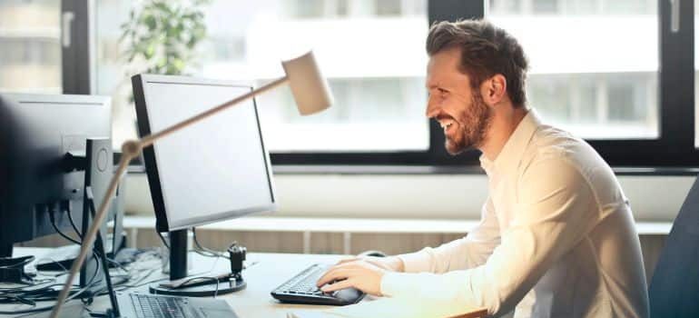 Man sitting at a desk next to a large window in an office and writing an email