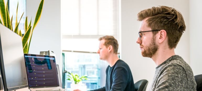 Two men sitting next to each other and working on their laptops