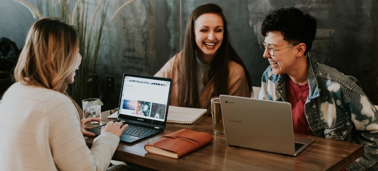Three women sitting at a table and reading customer reviews on their laptops