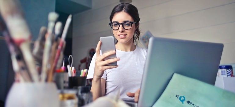 Person sitting in front of a laptop and using their smartphone