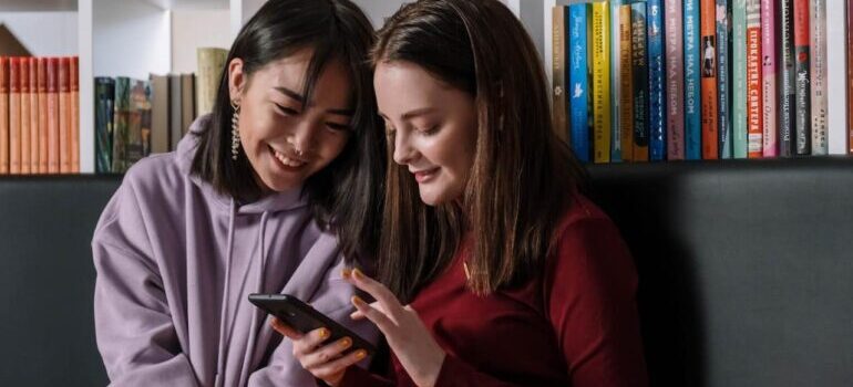 Two young women sitting on a couch and researching marketing moving services to Millennials and GenZ on their phones