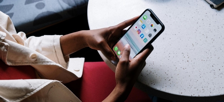 erson using a smartphone with various social media apps open on the screen while sitting at a table.