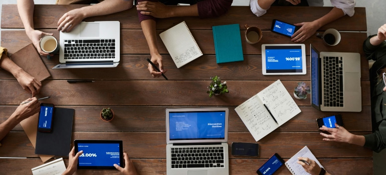 Team meeting with laptops and tablets, illustrating how advertising can pull your moving company through economic challenges.