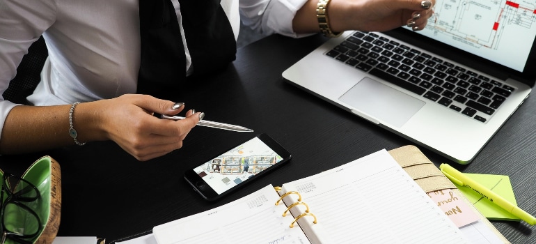 A businessperson working at a desk with a laptop, smartphone, and open planner, discussing market shifts and your moving business strategies.