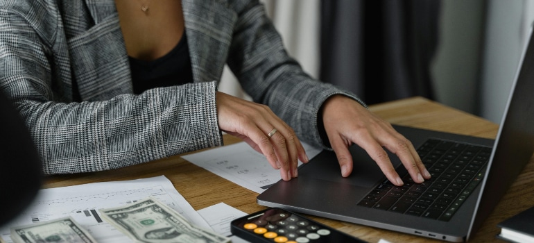 Business professional calculating budget on a laptop with dollar bills and calculator on the table, illustrating how much should movers spend on Facebook Ads.