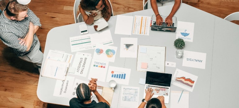 A group of professionals gathered around a table covered with charts, graphs, and strategy documents.