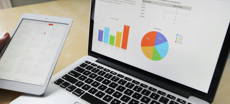 An open laptop displaying charts and graphs alongside a calendar on a tablet, illustrating the analysis of seasonal trends in moving.