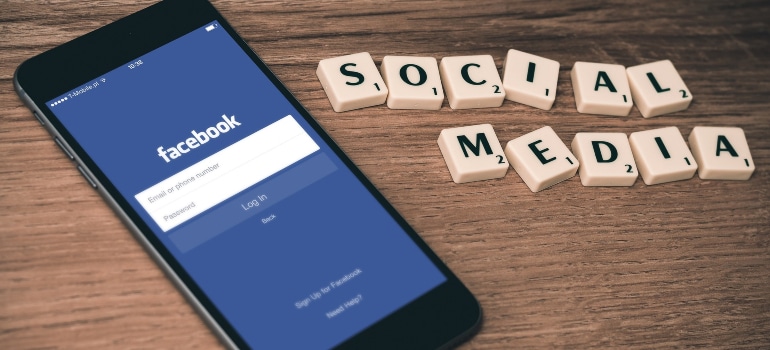 Smartphone displaying the Facebook login screen next to Scrabble tiles spelling 'Social Media.'