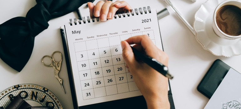 A person marking dates on a May 2021 calendar, highlighting the importance of planning based on seasonal trends in moving.