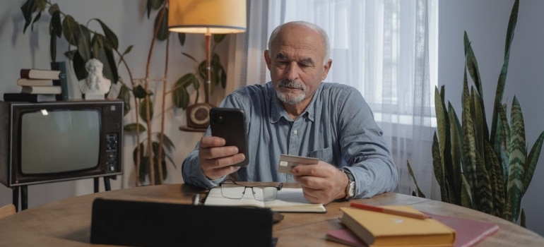 an old man holding a mobile phone and a credit card 